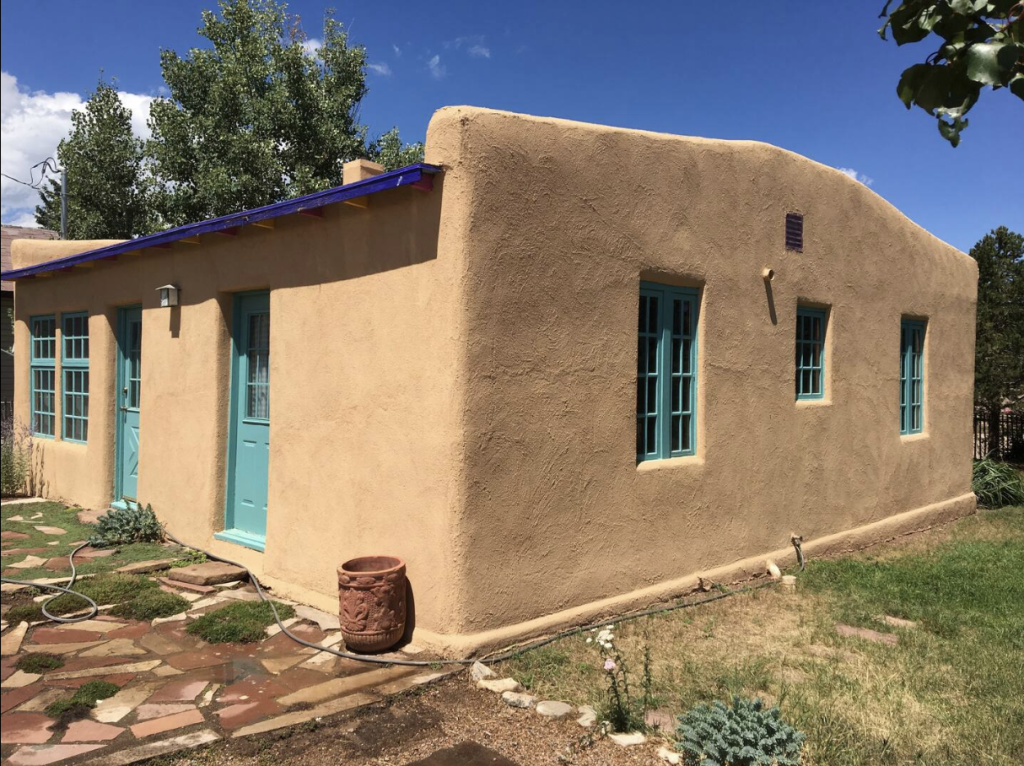 Colorado Mountain Property and Homes for Sale - Discover a charming adobe Airbnb house with a turquoise door and window frames, set against a clear blue sky in Southern Colorado, surrounded by a natural landscape.